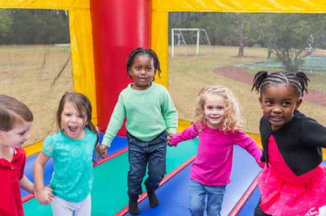 Children holding hands and smiling while playing inside a colorful bounce house.